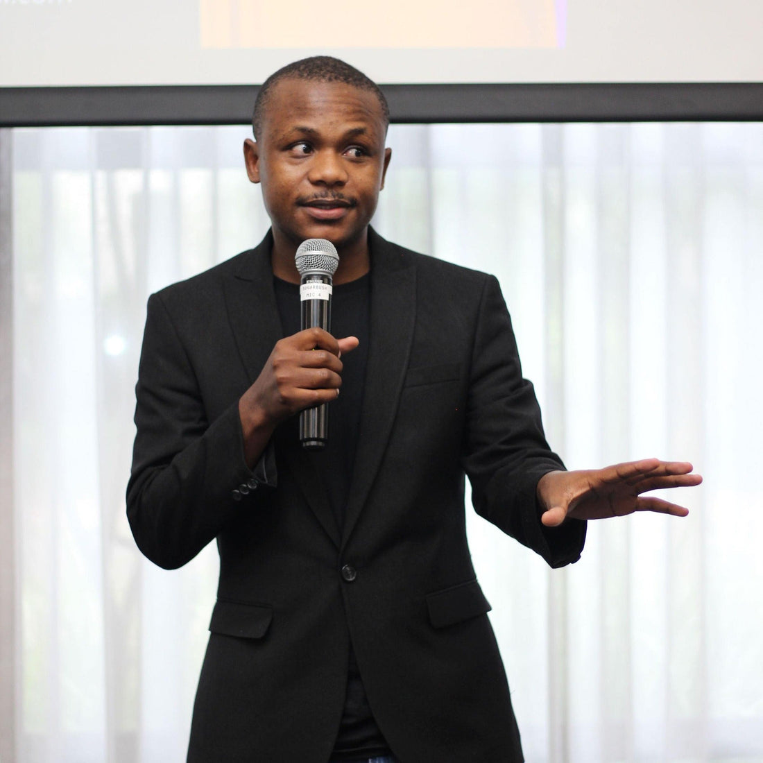 Ndivhuwo Muhanelwa speaking on stage with a microphone